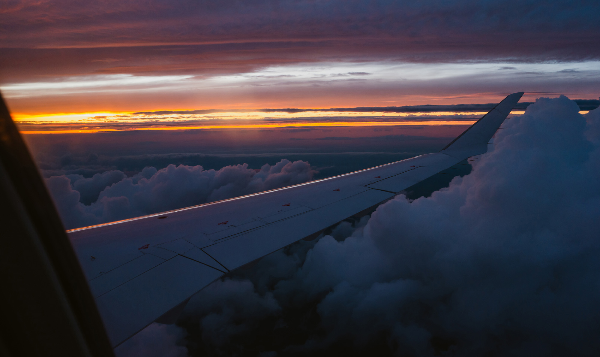 View outside of an airplane window of the wing, sunset, and clouds
