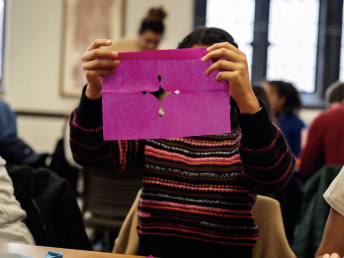 A student evaluates the first cuts to a sheet of papel picado.