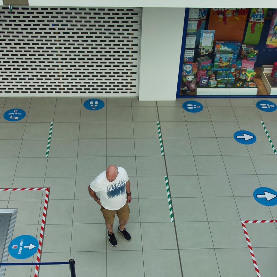 Interior of a shopping mall with one person marked with social distancing stickers