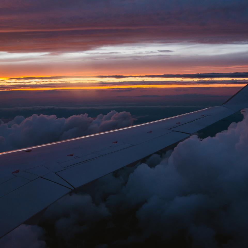 View outside of an airplane window of the wing, sunset, and clouds