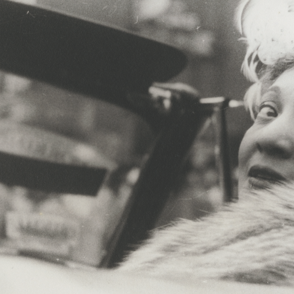 Gerri Major in a convertible looking back and wearing a fur stole.
