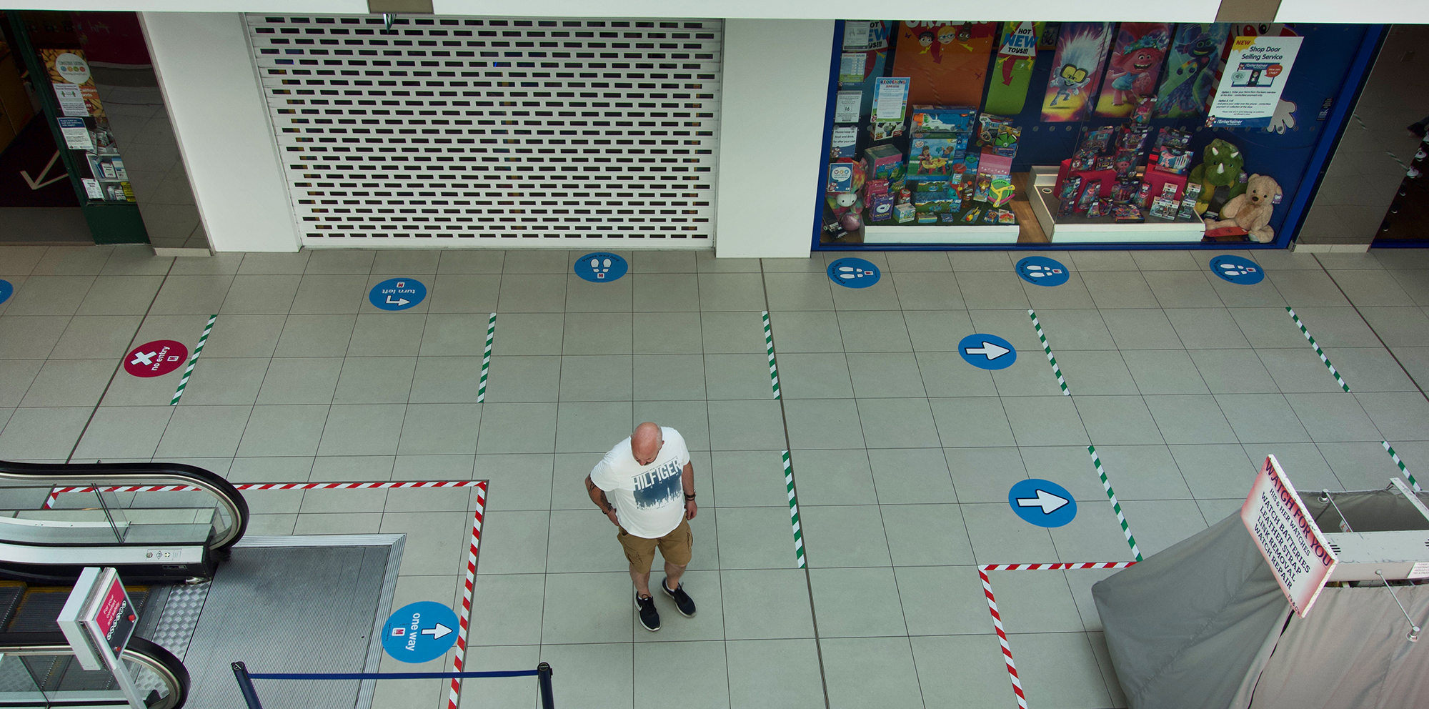 Interior of a shopping mall with one person marked with social distancing stickers