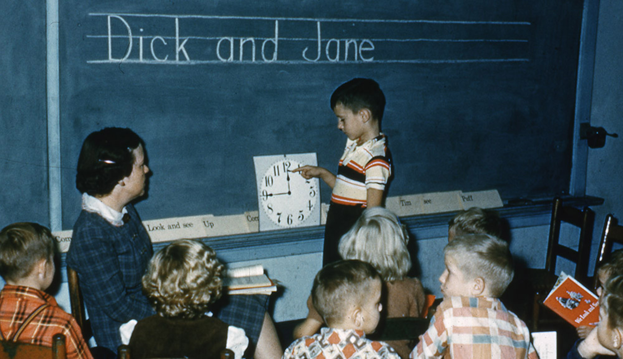 A child at a blackboard while the teacher and other students look on 