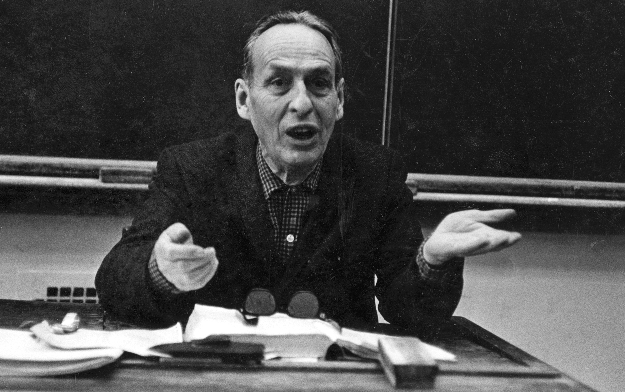 Norman Maclean sitting at a desk in classroom teaching