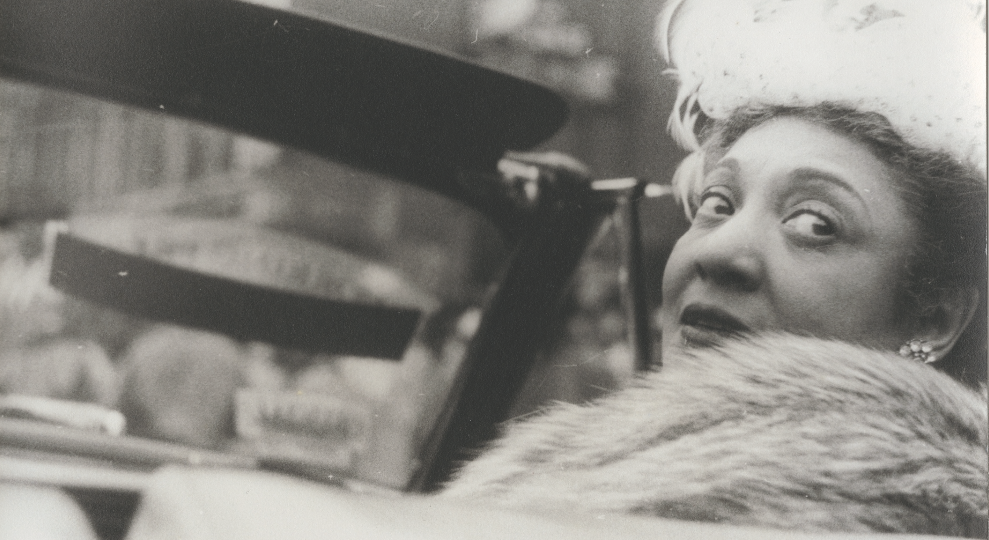 Gerri Major in a convertible looking back and wearing a fur stole.
