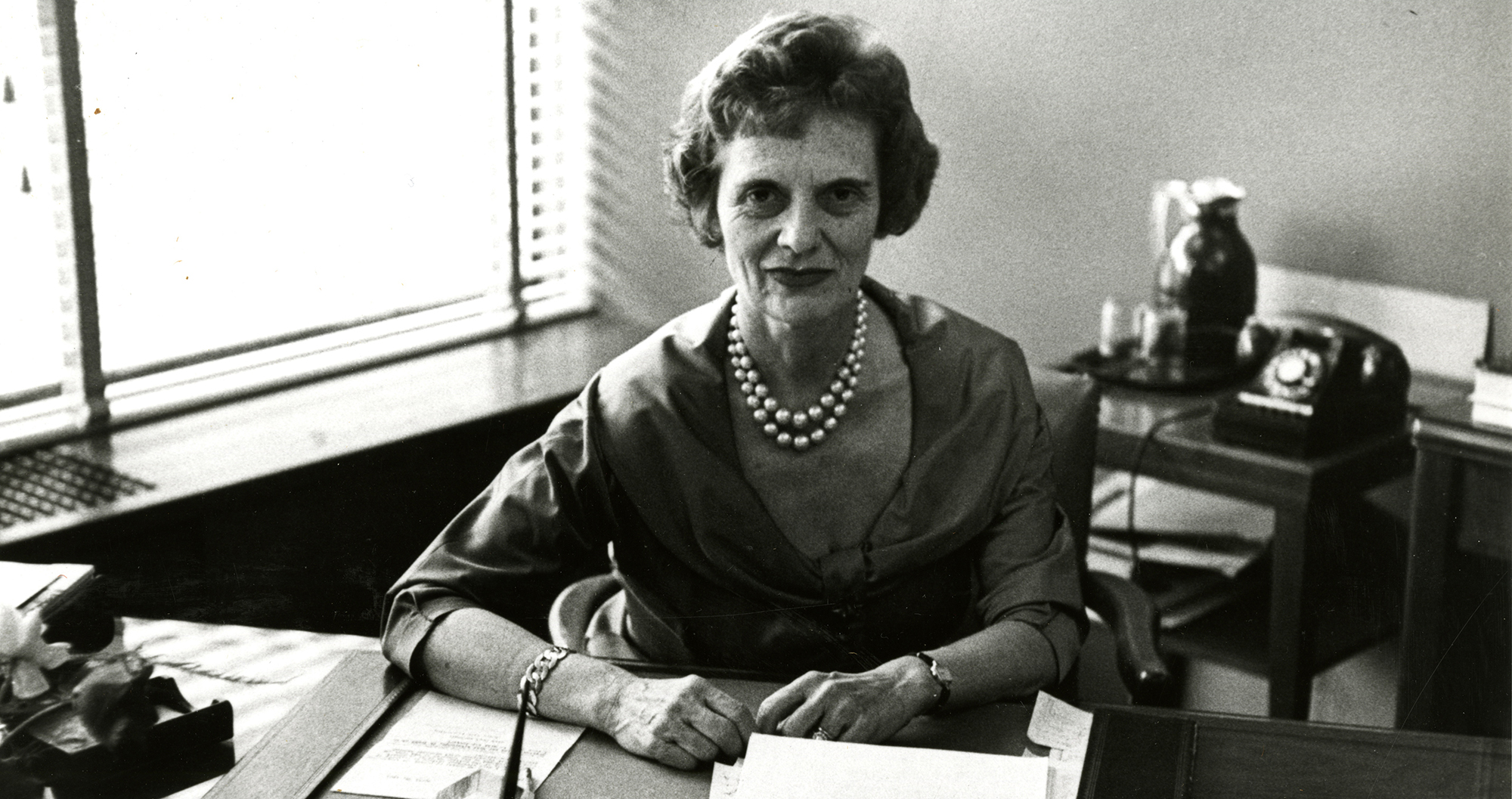 Black and white photo of mathematician Mina Rees sitting at her desk
