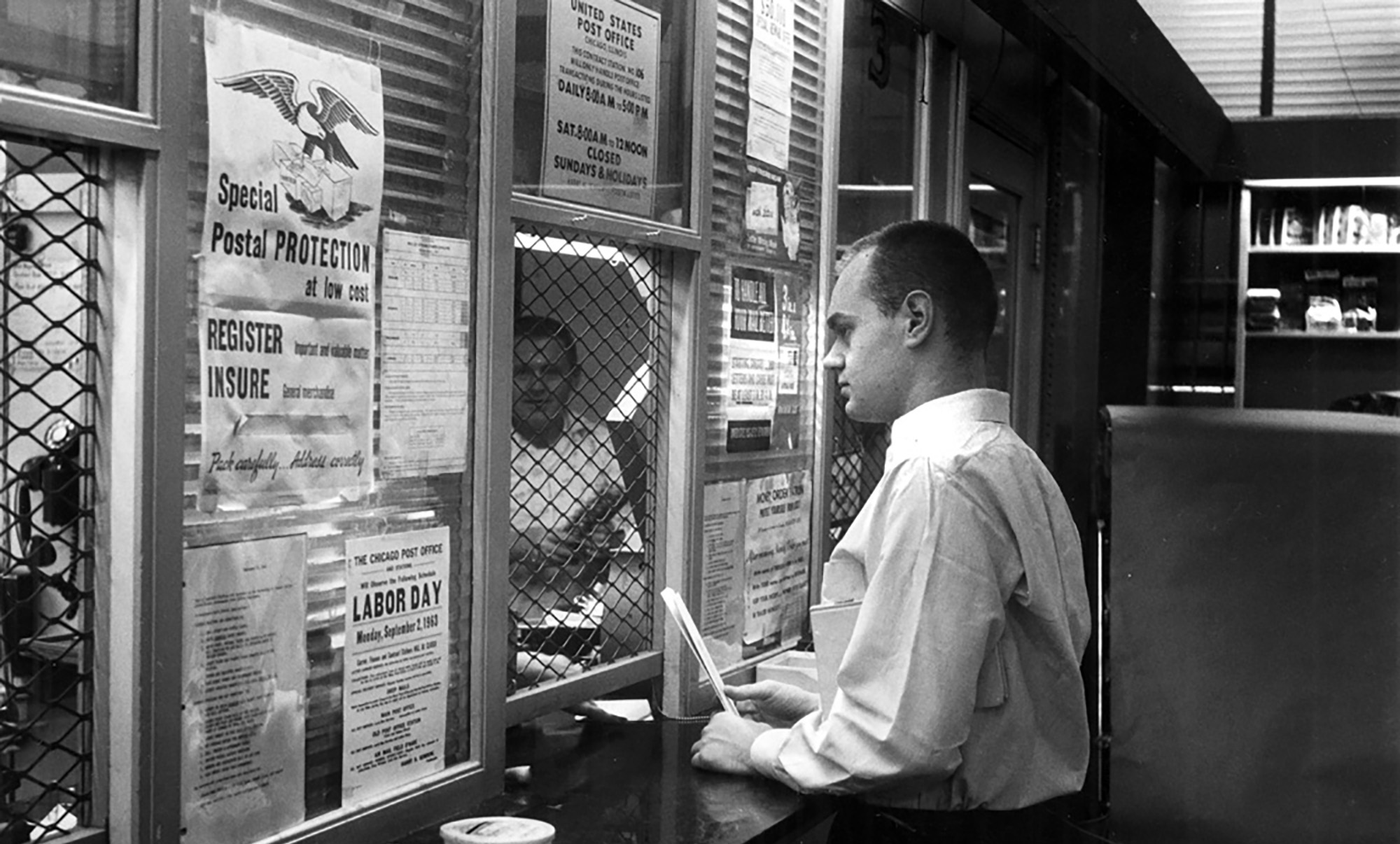 A man in a white shirt stands at the counter at the post office in the University Bookstore in 1963