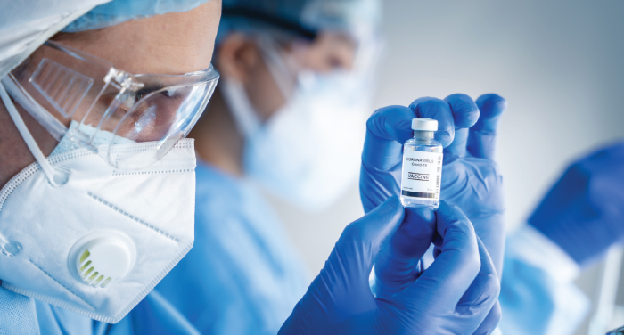 A person in PPE holding a vial of COVID-19 vaccine