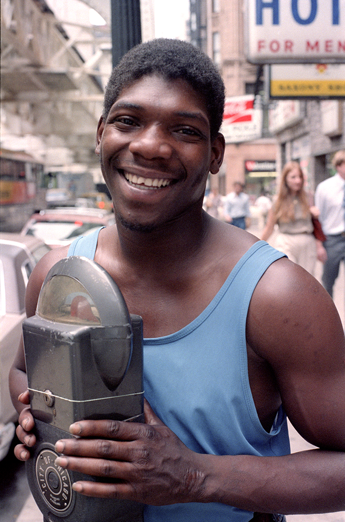 A young man stands by a parking meter on a Chicago sreet in the 1980s