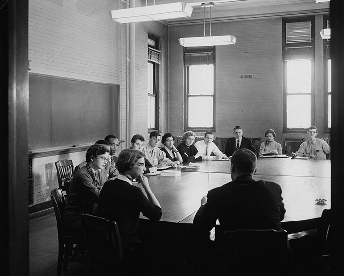 A group of college students sitting around a large table in a classroom in 1956