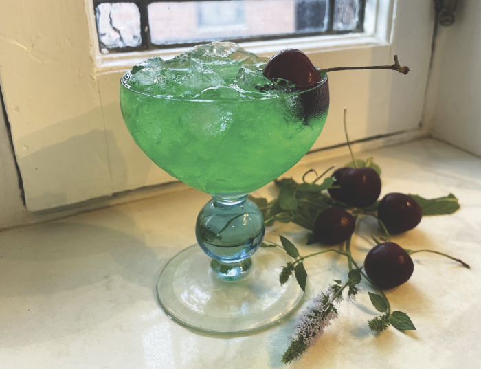 A green cocktail in a vintage glass with lots of ice and a cherry.