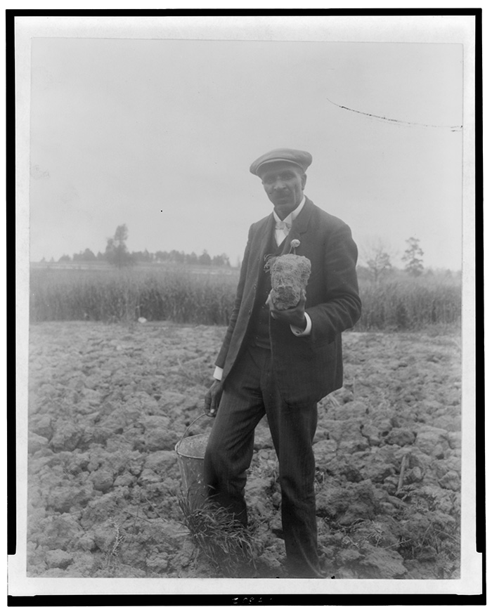 George Washington Carver in a field holding a pail and a large clump of the Tuskegee soil he used in his blue pigment