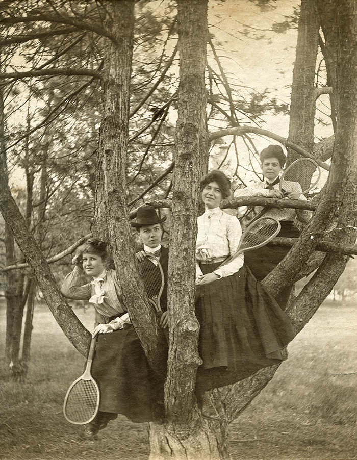 Four women holding tennis rackets sit in a tree